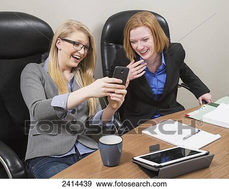 Stock Photograph - Co-workers laughing about a social media message; Edmonton, Alberta, Canada. Fotosearch - Search Stock Photography, Posters, Pictures, and Photo Clipart Images