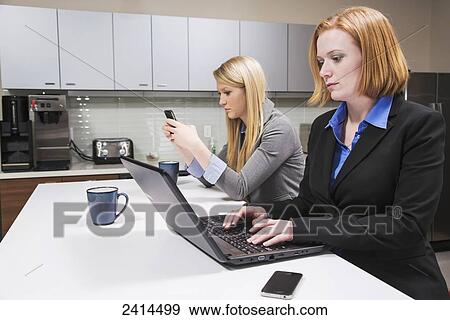 Stock Photo - Co-workers on a break, texting and working on a computer; Edmonton, Alberta, Canada. Fotosearch