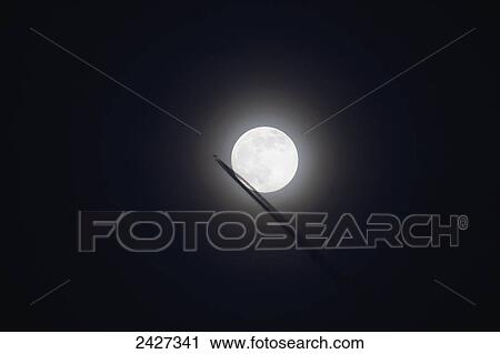 Stock Image - Commercial jet leaves a vapor trail as it flies past the full moon; Prescott, Arizona, United States of America. Fotosearch