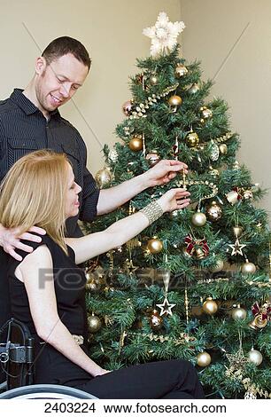 Couple decorating a Christmas tree together with wife in a wheelchair; Edmonton, Alberta, Canada View Large Photo Image Picture - Couple decorating a Christmas tree together with wife in a wheelchair; Edmonton, Alberta, Canada. Fotosearch
