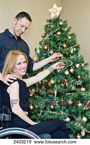 Couple decorating a Christmas tree together with wife in a wheelchair; Edmonton, Alberta, Canada View Large Photo Image Stock Photo - Couple decorating a Christmas tree together with wife in a wheelchair; Edmonton, Alberta, Canada. Fotosearch
