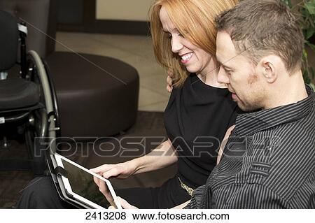 Stock Photo - Couple looking a tablet together, wife with a disability; Edmonton, Alberta, Canada. Fotosearch