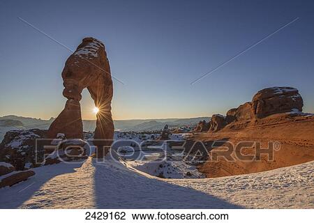 Stock Image - Evening sun shines through Delicate Arch, Arches National Park; Utah, United States of America. Fotosearch