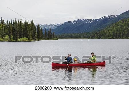 Stock Image - Family in red canoe on Byers Lake with green tree covered hills and Talkeetna Mountains in the background, Denali State Park; Alaska, Alaska, United States of America. Fotosearch