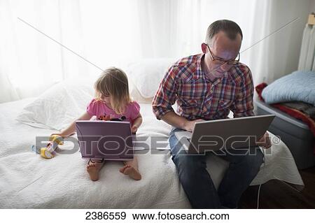 Stock Photo - Father and daughter at home working on their laptops; Toronto, Ontario, Canada. Fotosearch