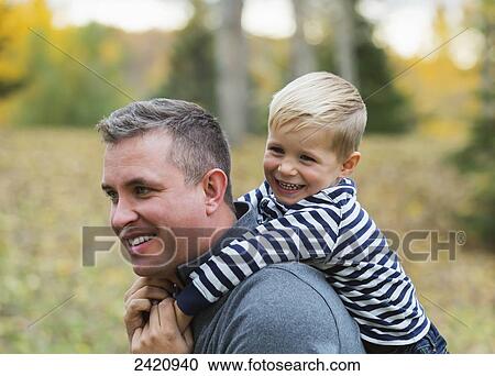 Stock Image - Father carrying his young son on his back in a park in autumn; Edmonton, Alberta, Canada. Fotosearch