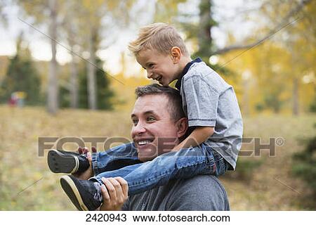 Father carrying his young son on his shoulders in a park in autumn; Edmonton, Alberta, Canada View Large Photo Image Stock Image - Father carrying his young son on his shoulders in a park in autumn; Edmonton, Alberta, Canada. Fotosearch