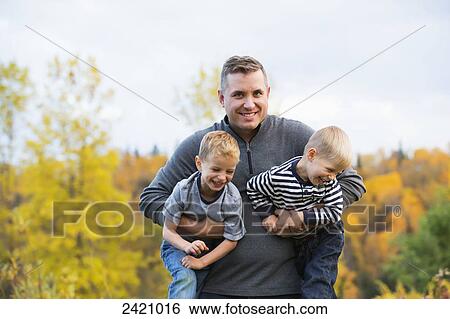 Father carrying two young sons in a park in autumn; Edmonton, Alberta, Canada View Large Photo Image Stock Photograph - Father carrying two young sons in a park in autumn; Edmonton, Alberta, Canada. Fotosearch