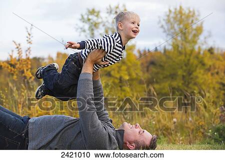 Stock Image - Father holding his son high in the air pretending to fly; Edmonton, Alberta, Canada. Fotosearch