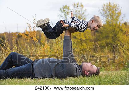 Stock Photo - Father holding his son high in the air pretending to fly; Edmonton, Alberta, Canada. Fotosearch