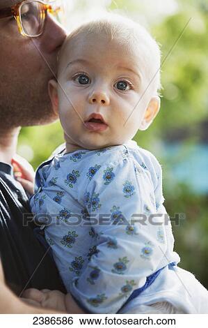 Stock Photograph - Father holds and kisses young baby boy; Toronto, Ontario, Canada. Fotosearch