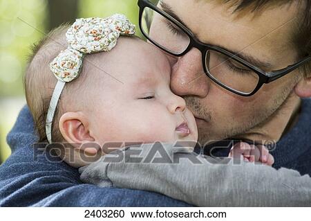 Stock Image - Father kissing his infant daughter while she sleeps; Edmonton, Alberta, Canada. Fotosearch