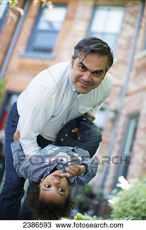 Stock Image - Father playing with son and holding him upside down; Toronto, Ontario, Canada. Fotosearch