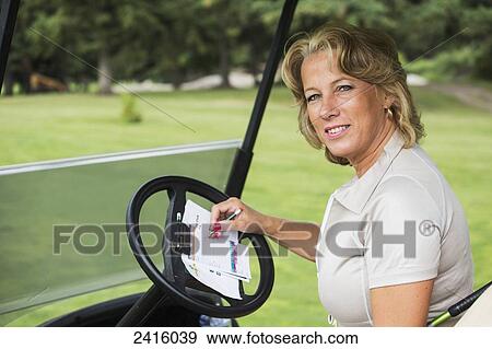 Stock Photo - Female golfer writing on a score card in a golf cart; Edmonton, Alberta, Canada. Fotosearch