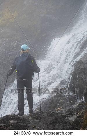 Stock Photo - Female hiker on rocky trail in fog next to waterfalls flowing over rocky cliff face; Lanserbach, Austria. Fotosearch