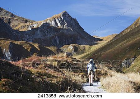 Stock Photo - Female hiker on trail with grass covered slopes and mountain peak; Hintertux, Austria. Fotosearch