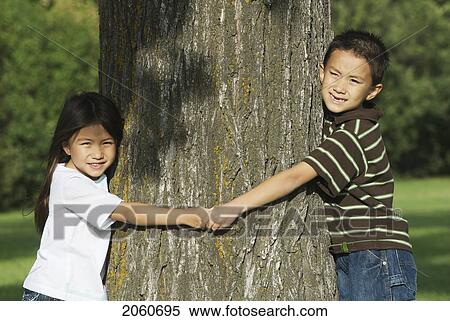 Stock Photography - Five Year Old Sister And Seven Year Old Brother Hold Hands Around Tree, Winnipeg, Canada. Fotosearch