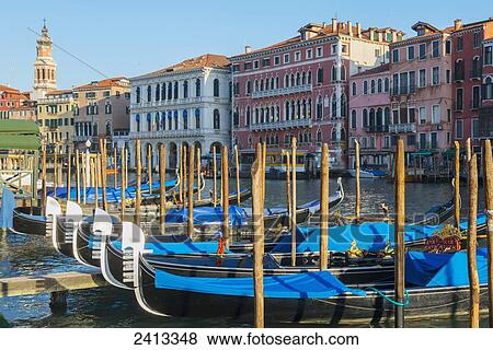 Gondolas mooring in a row in the canal with colourful buildings along the shoreline; Venice, Italy View Large Photo Image Stock Photo - Gondolas mooring in a row in the canal with colourful buildings along the shoreline; Venice, Italy. Fotosearch