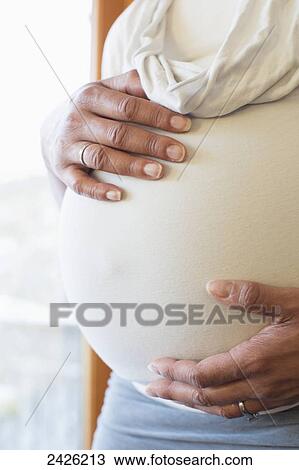 Stock Image - Hands of a woman on her pregnant belly; Toronto, Ontario, Canada. Fotosearch