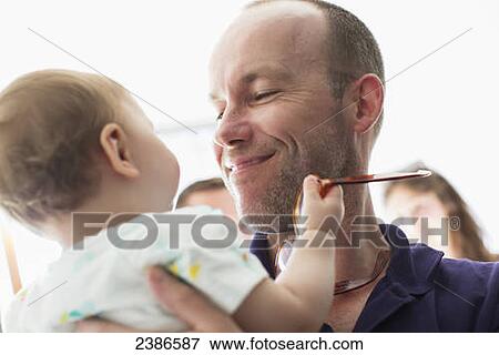 Stock Photo - Happy man holding a one year old baby holding his glasses; Toronto, Ontario, Canada. Fotosearch