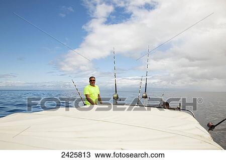 Stock Image - Hawaii, Maui, Man poses with poles on fishing boat. Fotosearch