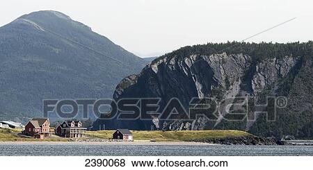 Stock Photo - Houses and a cliff along the water's edge of Bonne Bay; Newfoundland and Labrador, Canada . Fotosearch