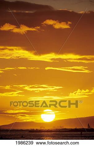 Stock Photo - Huge Sunball In Yellow Sunset Sky, About To Set Behind Land And Ocean.. Fotosearch