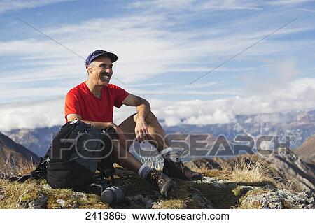 Male hiker sitting on top of grassy mountain top with mountain range in the distance and blue sky and clouds; Hinterux, Austria View Large Photo Image Stock Photography - Male hiker sitting on top of grassy mountain top with mountain range in the distance and blue sky and clouds; Hinterux, Austria. Fotosearch