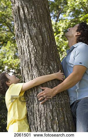 Stock Image - Man And Boy Hold Trunk Of Tree, Looking Upward, Winipeg, Canada. Fotosearch