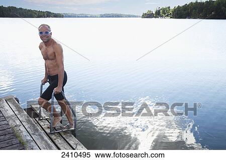 Stock Photography - Man getting out of the water onto a dock; Morbylanga, Sweden. Fotosearch