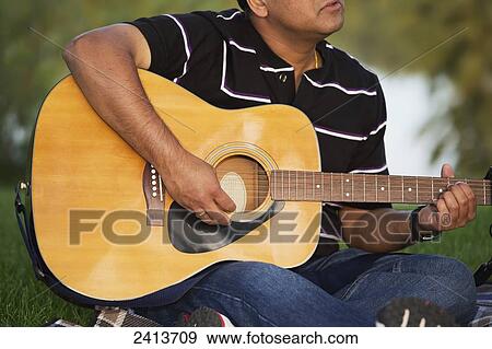 Stock Photo - Man playing his guitar outdoors; Edmonton, Alberta, Canada. Fotosearch