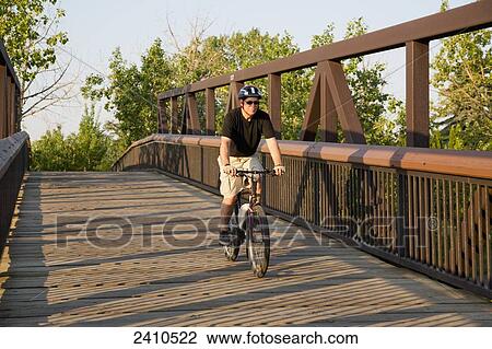 Stock Image - Man riding his electric bicycle over a bridge; Edmonton, Alberta, Canada. Fotosearch