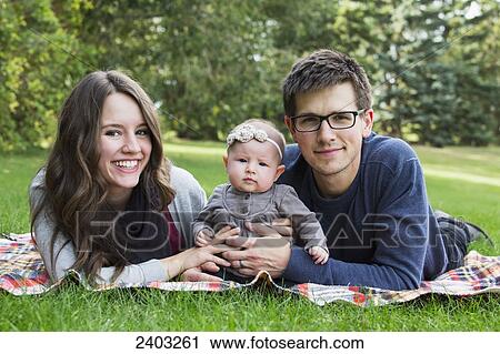 Stock Image - Married couple with an infant daughter in a park; Edmonton, Alberta, Canada. Fotosearch