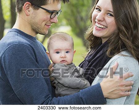 Stock Image - Married couple with infant daughter in a park; Edmonton, Alberta, Canada. Fotosearch