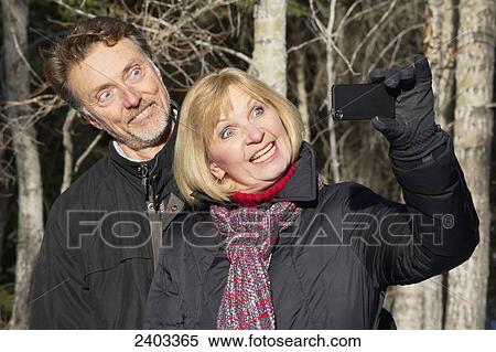 Stock Photography - Mature couple taking a self-portrait with their camera in a forest; Canmore, Alberta, Canada. Fotosearch