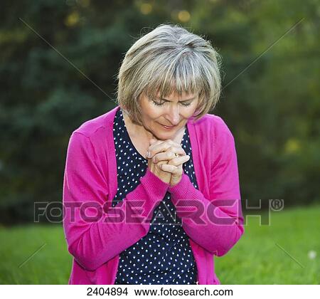 Picture - Mature woman praying in the park; Edmonton, Alberta, Canada. Fotosearch