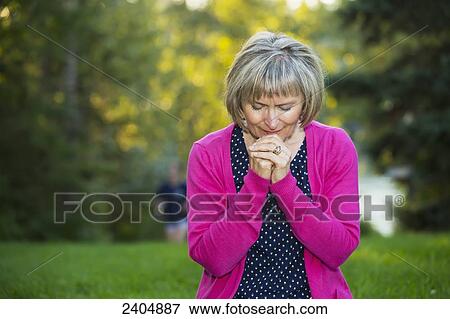 Stock Photo - Mature woman praying in the park; Edmonton, Alberta, Canada. Fotosearch