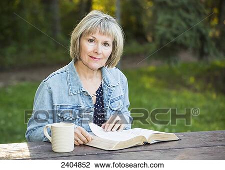 Stock Image - Mature woman reading her Bible in the park; Edmonton, Alberta, Canada. Fotosearch