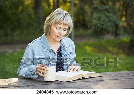 Stock Photography - Mature woman reading her Bible in the park; Edmonton, Alberta, Canada. Fotosearch