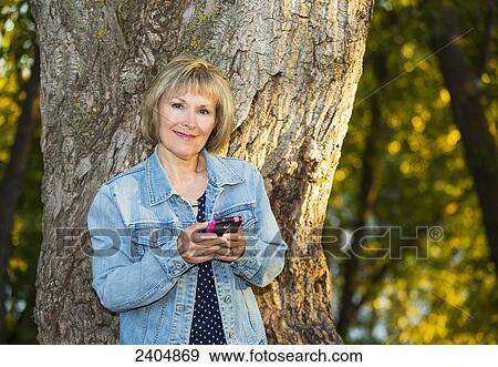 Mature woman using a cell phone in the park; Edmonton, Alberta, Canada View Large Photo Image Stock Photo - Mature woman using a cell phone in the park; Edmonton, Alberta, Canada. Fotosearch