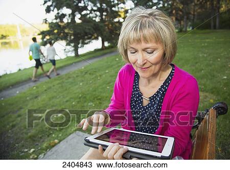 Mature woman using a tablet in a city park; Edmonton, Alberta, Canada View Large Photo Image Stock Image - Mature woman using a tablet in a city park; Edmonton, Alberta, Canada. Fotosearch