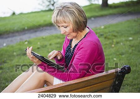 Mature woman using a tablet in a city park; Edmonton, Alberta, Canada View Large Photo Image Stock Photo - Mature woman using a tablet in a city park; Edmonton, Alberta, Canada. Fotosearch