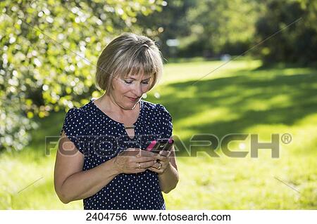 Mature woman using cell phone in a park; Edmonton, Alberta, Canada View Large Photo Image Stock Photograph - Mature woman using cell phone in a park; Edmonton, Alberta, Canada. Fotosearch