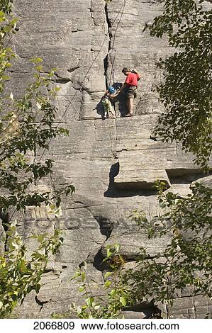 Stock Photo - Mid-Age Man Climbing With Daughter (Age 5) Up Granite Cliff At Stone Hills Near Rexford, Montana, Usa. Fotosearch