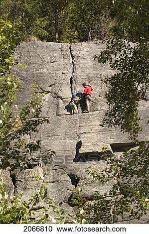 Stock Image - Mid-Aged Man Helping Daughter Tie Climbing Rope At Base Of Cliff, Near Rexford, Montana, Usa. Fotosearch