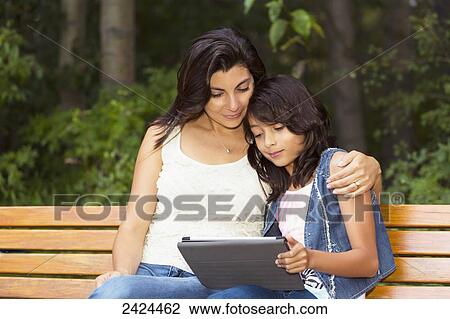 Mother and daughter looking at a tablet on a park bench; Edmonton, Alberta, Canada View Large Photo Image Stock Image - Mother and daughter looking at a tablet on a park bench; Edmonton, Alberta, Canada. Fotosearch