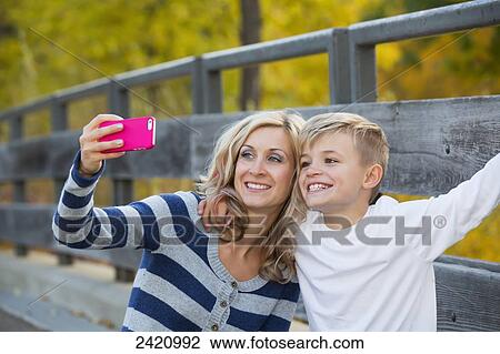 Mother and son using a smart phone to take a self-portrait in a park in autumn; Edmonton, Alberta, Canada View Large Photo Image Stock Image - Mother and son using a smart phone to take a self-portrait in a park in autumn; Edmonton, Alberta, Canada. Fotosearch