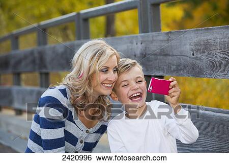Mother and son using a smart phone to take a self-portrait in a park in autumn; Edmonton, Alberta, Canada View Large Photo Image Stock Photograph - Mother and son using a smart phone to take a self-portrait in a park in autumn; Edmonton, Alberta, Canada. Fotosearch
