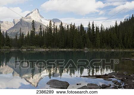 Mountain with sunlit peak reflecting in alpine lake with blue sky and clouds; British Columbia, Canada View Large Photo Image Stock Photo - Mountain with sunlit peak reflecting in alpine lake with blue sky and clouds; British Columbia, Canada . Fotosearch