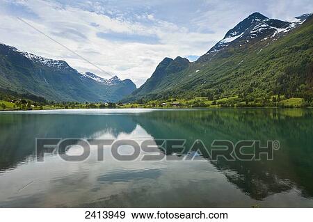 Stock Photo - Mountains and sky reflected in the tranquil water surrounded by mountains; Olden, Norway. Fotosearch